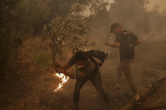 Les résidents locaux utilisent une branche d'arbre pour combattre les flammes lors d'un incendie de forêt dans le village de Pefki dans l'Eubée, en Grèce, le 8 août 2021.
