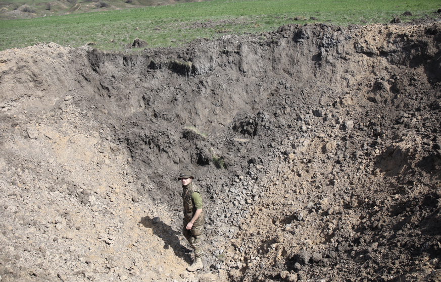 Un soldat dans le cratère causé par une bombe dans un champ.