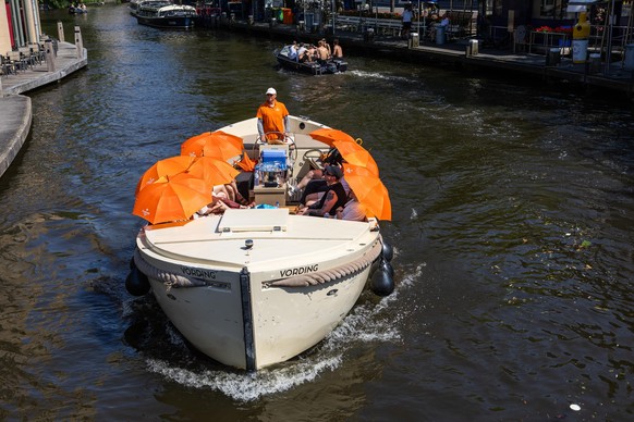 epa13049701 People shelter from the sun under umbrellas on a boat sailing through the canal in Amsterdam's city center, the Netherlands, 19 June 2026. Due to the warm weather, the National Heat P ...