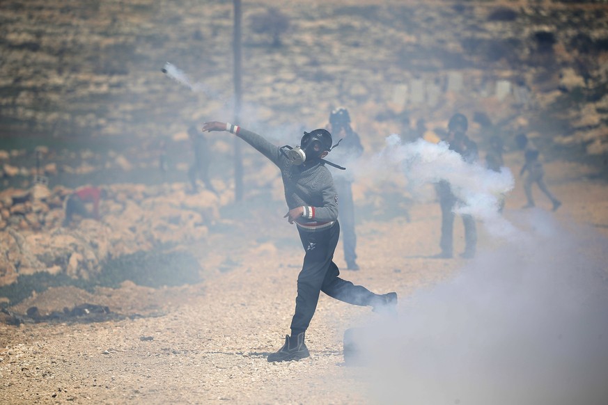 epa10488293 A Palestinian throws back a tear gas grenade during clashes with Israeli soldiers after a protest at Bet Dajan village near the West Bank city of Nablus, 24 February 2023. Palestinians pro ...