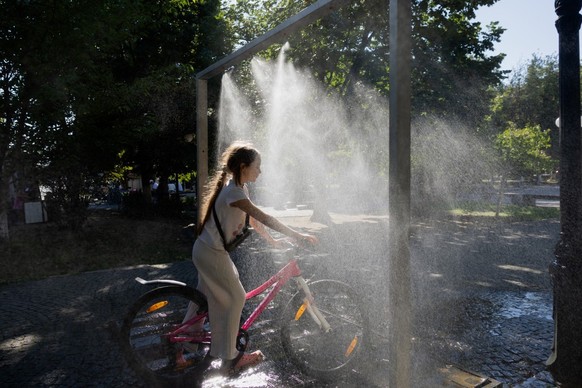 (FILES) A girl rides a bicyle under a water sprinkler in Berehove on August 28, 2026, amid the Russian invasion of Ukraine. Nestled in the foothills of the Carpathian mountains and tucked between Slov ...