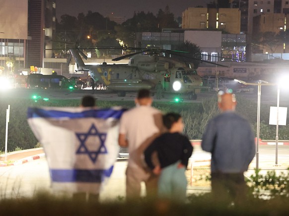 Des personnes avec un drapeau israélien regardent un hélicoptère militaire ramenant des enfants otages de la bande de Gaza et atterrissant sur l&#039;héliport d&#039;un centre médical à Petah Tikva, e ...