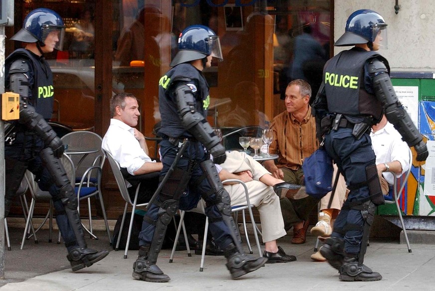 Guests of a sidewalk cafe look at police officers passing by, during clashes between anti-gloablisation demonstrators and riot police in Geneva, Switzerland, Tuesday, June 3, 2003. After the end of th ...