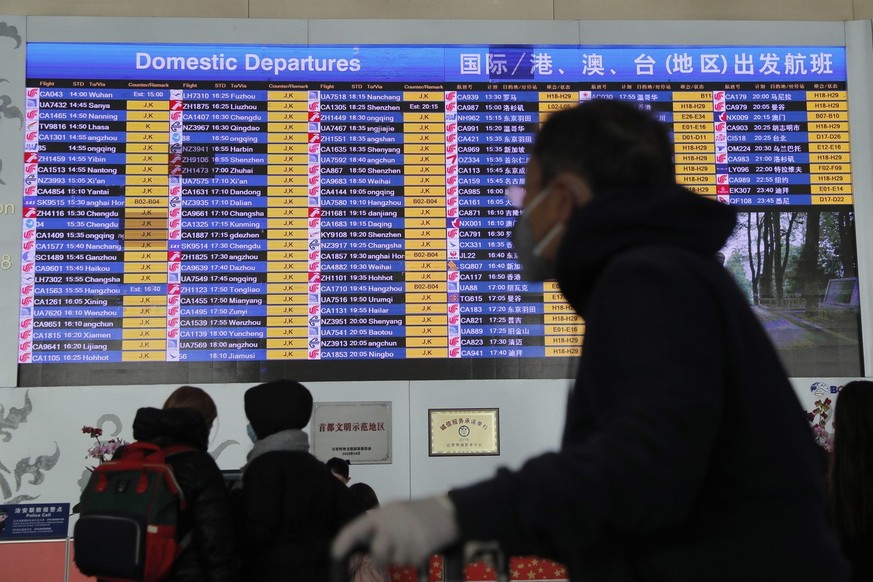 A passenger wears a mask passing by a departure information screen at terminal 3 of Beijing Capital International Airport in Beijing, China, 26 January 2020. Chinese official required all travel agenc ...