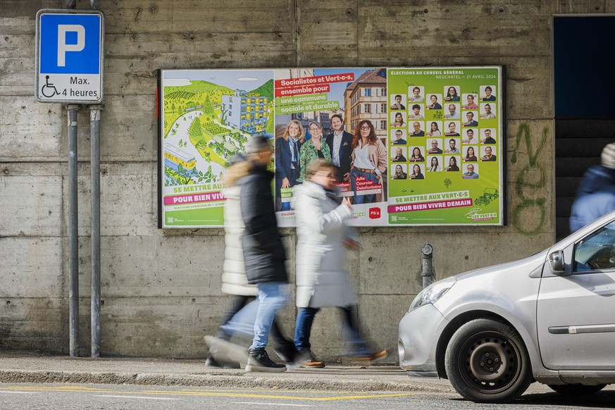 Des personnes marchent devant des affiches de campagne pour les elections communales neuchateloises du 21 avril prochain, ce samedi 23 mars 2024 a Neuchatel. (KEYSTONE/Valentin Flauraud)