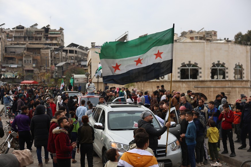 epa11762428 People wave a Syrian opposition flag after opposition fighters took control of the city of Hama, Syria, 07 December 2024. Syrian opposition forces, led by the Islamist militant group Hayat ...