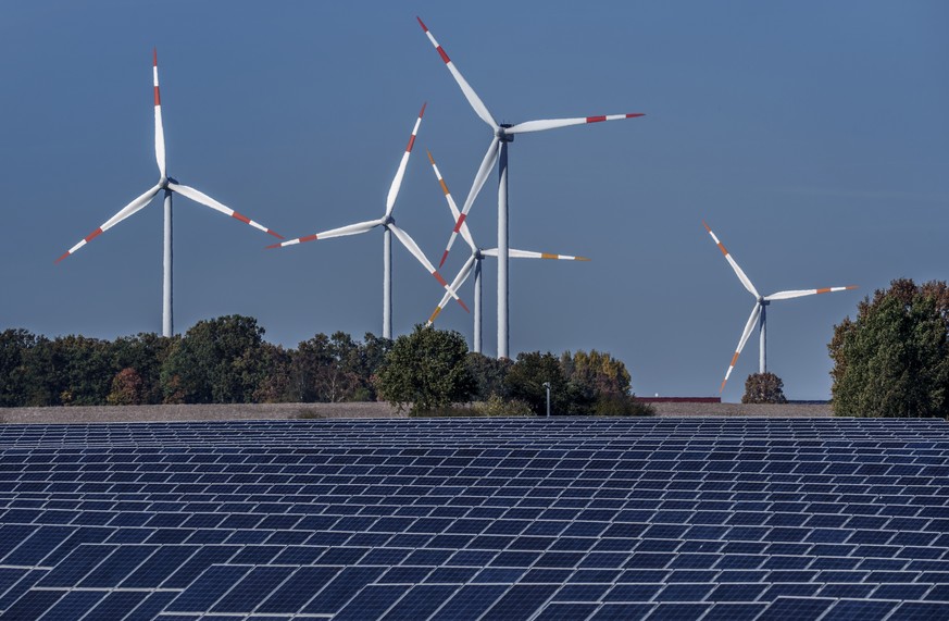 FILE - Wind turbines turn behind a solar farm in Rapshagen, Germany, Thursday, Oct. 28, 2021. Proponents of clean energy and thinks tanks have long said it's possible to reduce emissions and keep ...