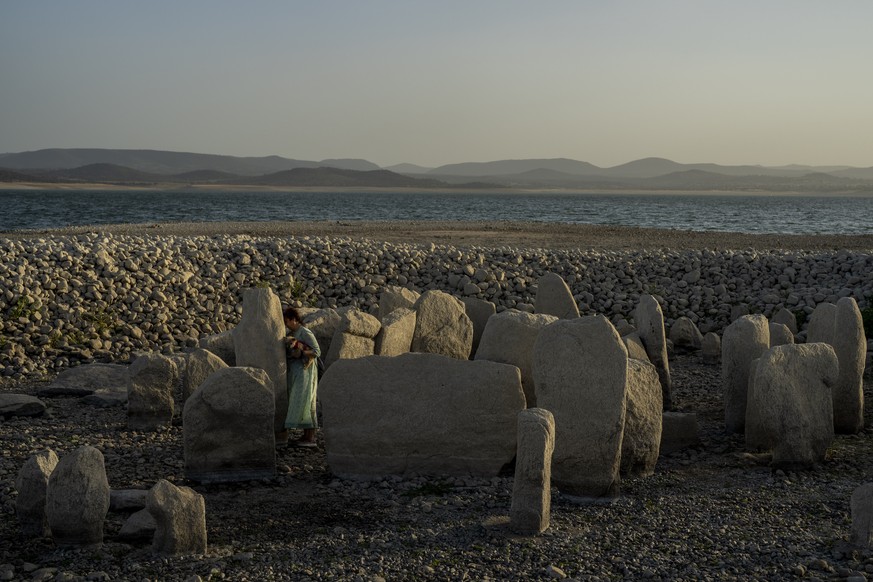 Amalie Garcia, 54, stands next to The Dolmen of Guadalperal, a megalithic monument that emerged due to drought at the Valdecanas reservoir in El Gordo, western Spain, Saturday, Aug. 13, 2022. In the w ...