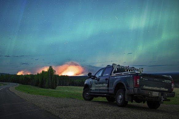 This photo provided by the Ministry of Water, Land and Resource Stewardship shows a wildfire, Aurora Borealis overhead, near Fort Nelson, British Columbia Saturday, May 11, 2024. An intense wildfire c ...