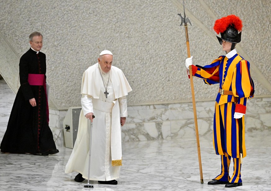 epa11246356 Pope Francis (C), using a cane, walks near a member of the Pontifical Swiss Guard as he arrives to lead his weekly general audience in the Paul VI Audience Hall in Vatican City, 27 March 2 ...