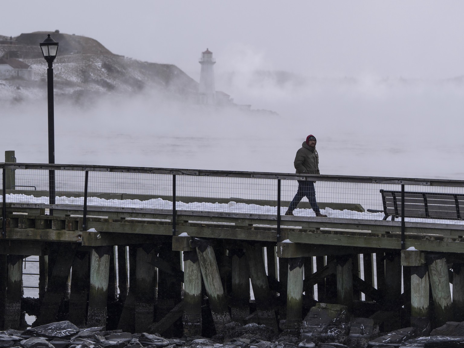 A man walks on the waterfront as sea smoke, or ice fog, forms in Halifax Harbor on Saturday, Feb. 4, 2023. Environment Canada has warned of windchill values between -30 C and -40 C across the Maritime ...