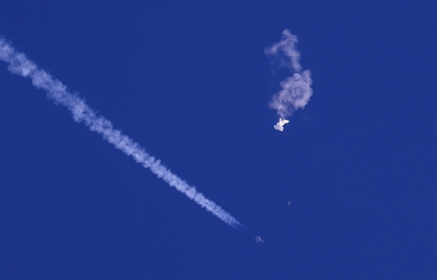 In this photo provided by Chad Fish, the remnants of a large balloon drift above the Atlantic Ocean, just off the coast of South Carolina, with a fighter jet and its contrail seen below it, Saturday,  ...