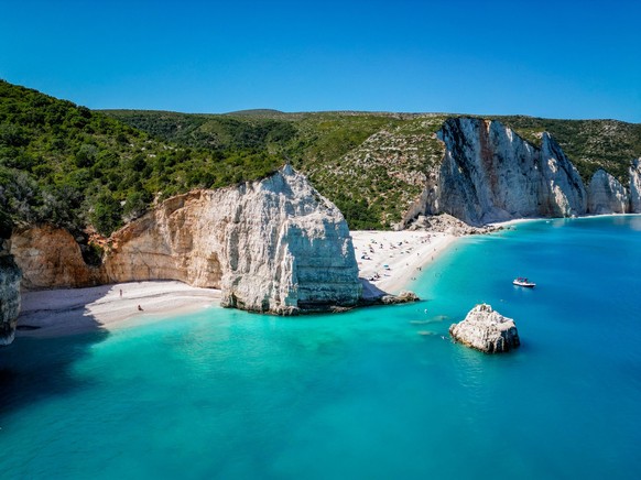 4K Angle shot of Fteri Beach, Kefalonia, Cephalonia, Greece showing little cove and main beach area, with rocky hillside, a boat and turquoise water xkwx aerial aquamarine background bay beautiful blu ...