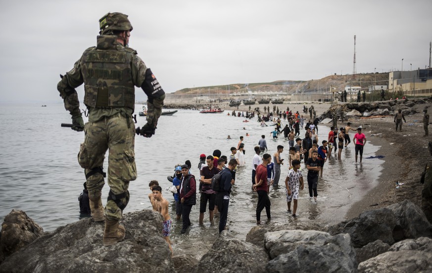 People mainly from Morocco stand on the shore as Spanish Army cordon off the area at the border of Morocco and Spain, at the Spanish enclave of Ceuta, on Tuesday, May 18, 2021. Ceuta, a Spanish city o ...