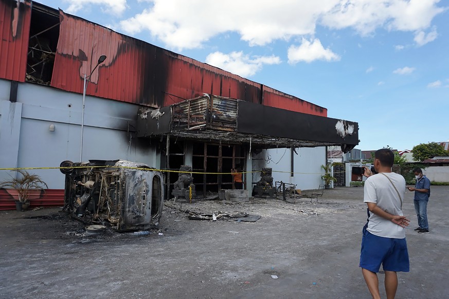 A man stands outside of a torched nightclub after two groups clashed in Sorong, West Papua province, Indonesia, Tuesday, Jan. 25, 2022. A fire engulfed the nightclub after two groups clashed inside th ...