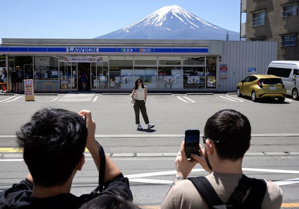 epa11330756 A foreign tourist poses for photographs in front of the Lawson Kawaguchiko Ekimae convenience store with Mount Fuji seen in the background, in Fujikawaguchiko, north of Mount Fuji, Japan,  ...