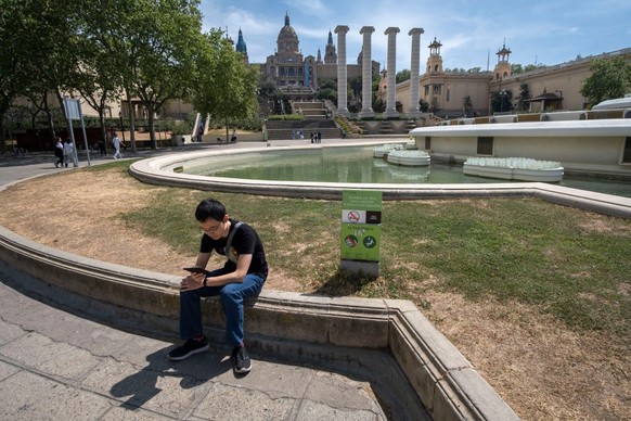 BARCELONA, CATALONIA, SPAIN - 2023/04/22: A tourist is seen sitting next to the informative poster of the pump stop as a measure to save water due to drought in La Fuente Mágica. After 30 months witho ...