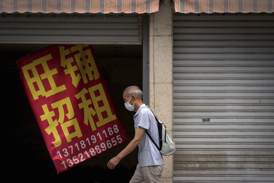 A man wearing a face mask walks by a banner that reads &quot;Prosperous shop for rent&quot; hangs on a vacant shop lot in Beijing, Wednesday, Aug. 17, 2022. Factories in China&#039;s southwest have sh ...