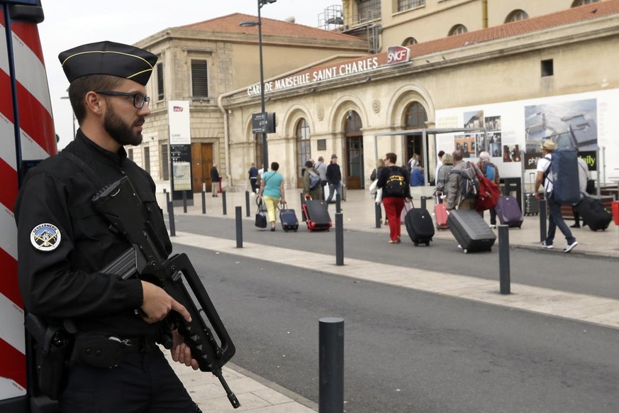 A police officer stands guard while passengers enter the Marseille Saint Charles train station, a day after a man fatally stabbed two women outside the train station, in Marseille, southern France, Mo ...