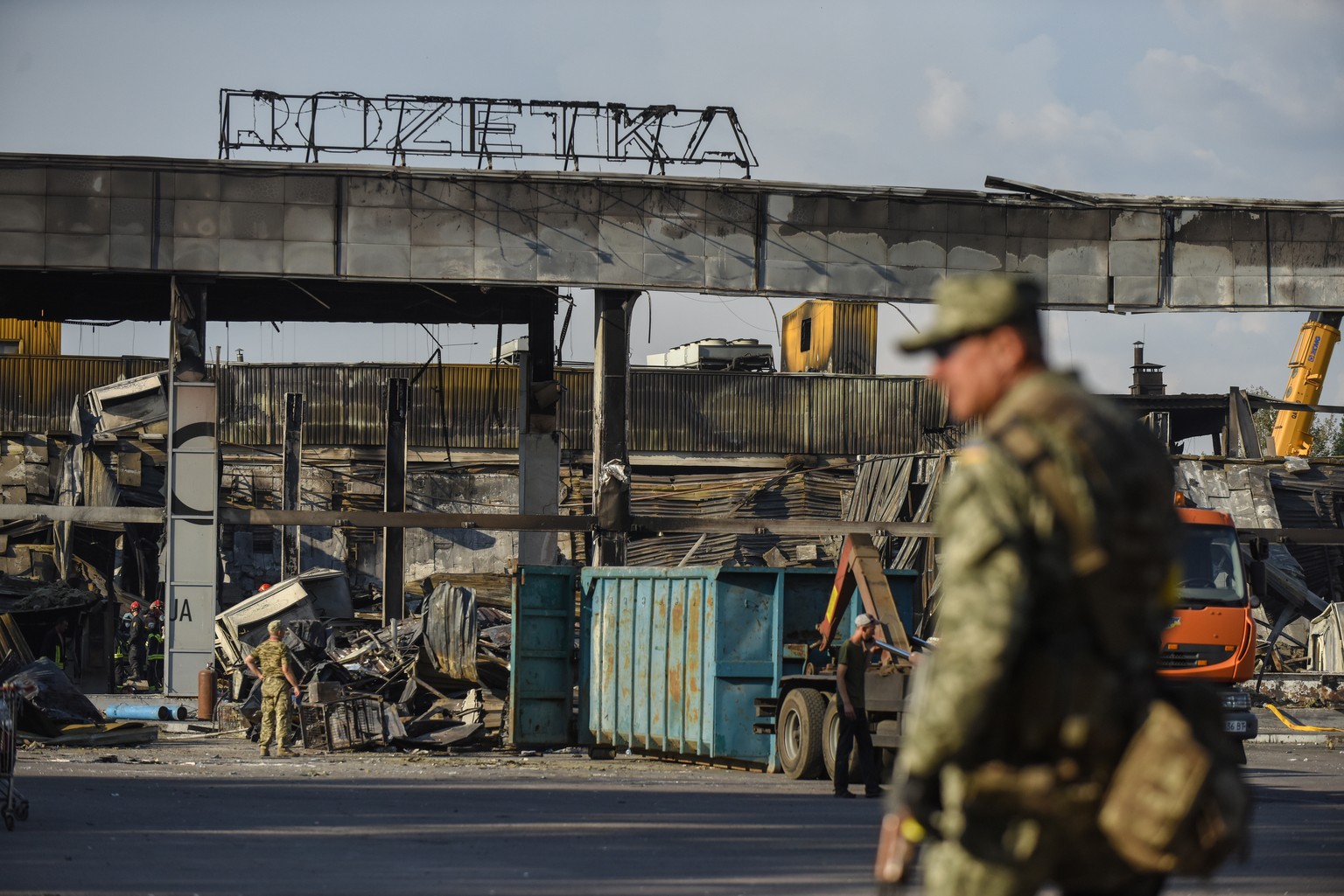 epa10039755 Ukrainian servicemen stand guard near the remains of the destroyed Amstor shopping mall in Kremenchuk, Ukraine, 28 June 2022. At least 18 people died following Russian airstrikes on the cr ...