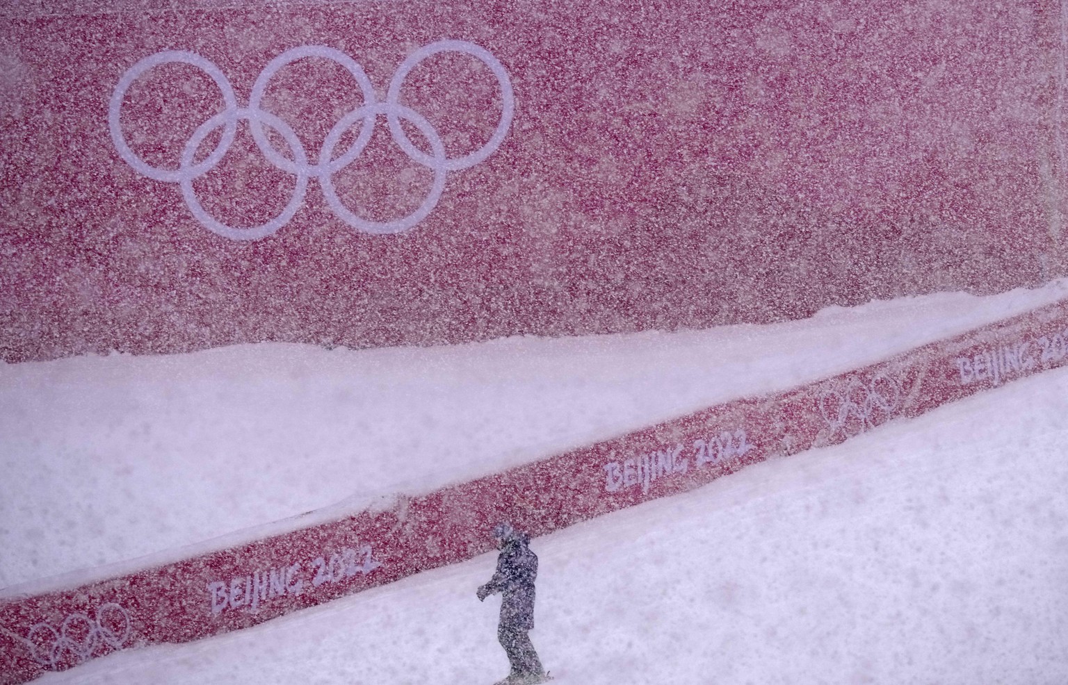 A course worker stands in the finish area of the men's giant slalom course as the snow comes down at the alpine ski venue at the 2022 Winter Olympics, Sunday, Feb. 13, 2022, in the Yanqing distri ...