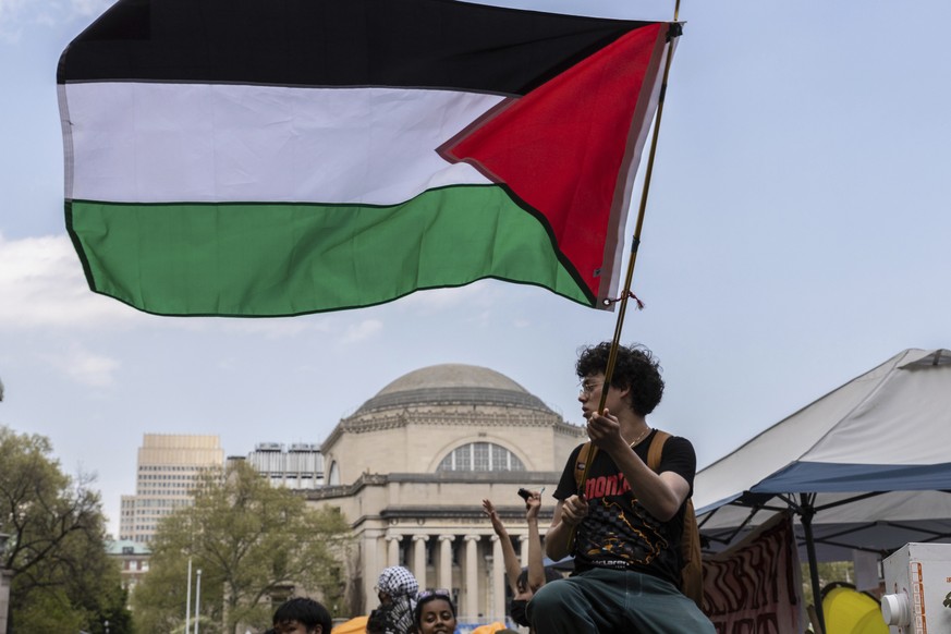A student protester waves a large Palestinian flag at their encampment on the Columbia University campus, Monday, April 29, 2024, in New York. Protesters of the war in Gaza who are encamped at Columbi ...