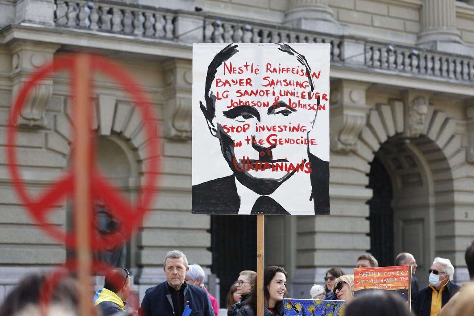 A protester holds a banners reading "Nestle Raiffeisen Bayer Samsung LG Sanofi Unilver Johnson & Johnson - Stop investing in the genocide of Ukrainians" during a demonstration against th ...