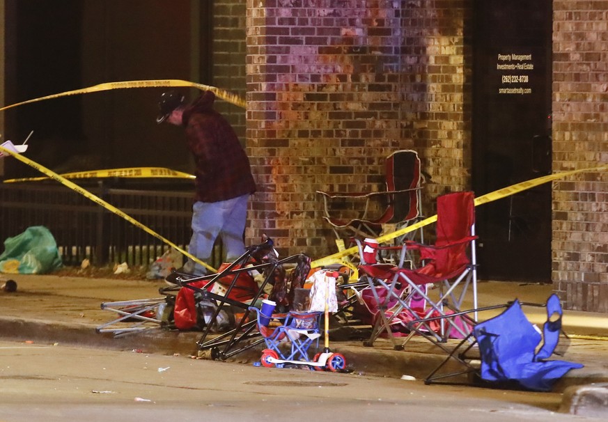 epa09597017 A man ducks under police tape as he walks past debris left from crowds attending a Christmas parade scattered along the route after a SUV reportedly broke through a barricade and drove int ...