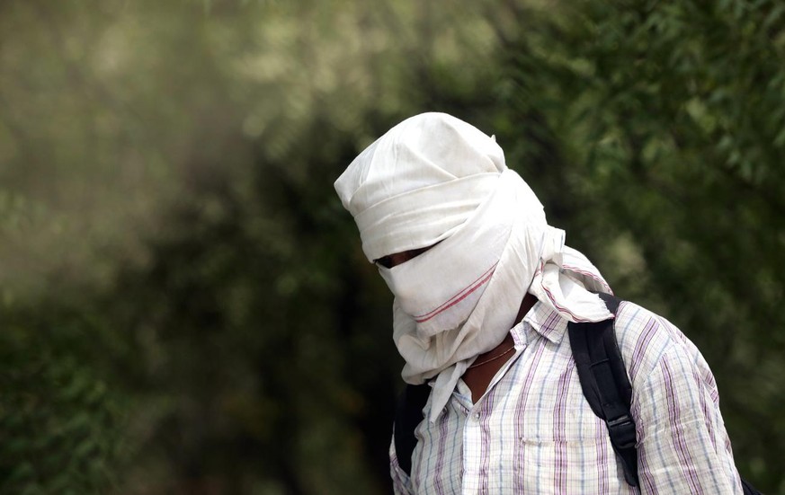 Un homme marche la tête couverte contre le soleil lors d'une chaude après-midi dans la banlieue de New Delhi, en Inde, le 1er mai 2022.