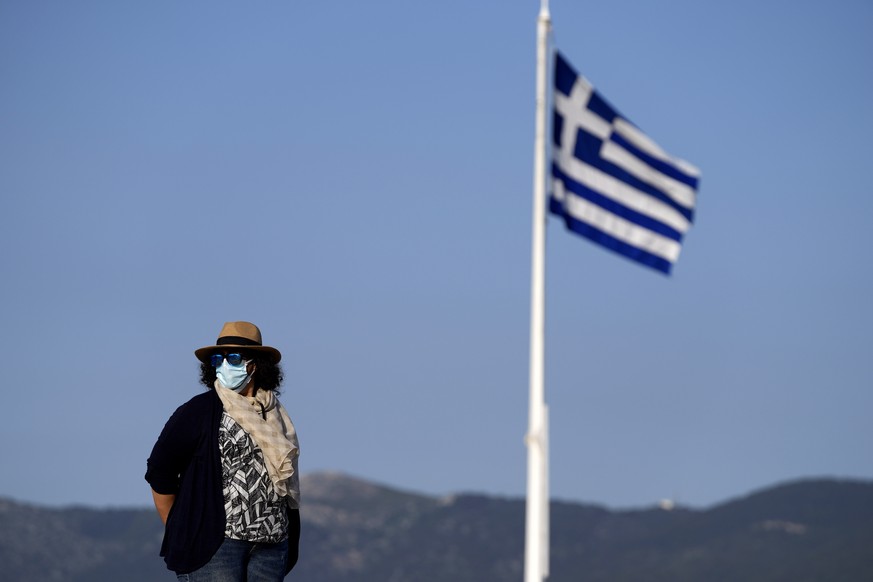 An employee of the Acropolis hill wearing protective face mask stands guard next of a Greek flag during a media tour for the Foreign Correspondents organised by the Greek Cultural Ministry at the Acro ...