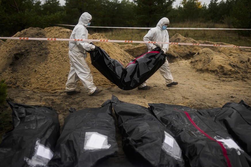 Members of a forensic team carry a plastic bag with a body inside as they work in an exhumation in a mass grave in Lyman, Ukraine, Tuesday, Oct. 11, 2022. This was the year war returned to Europe, and ...