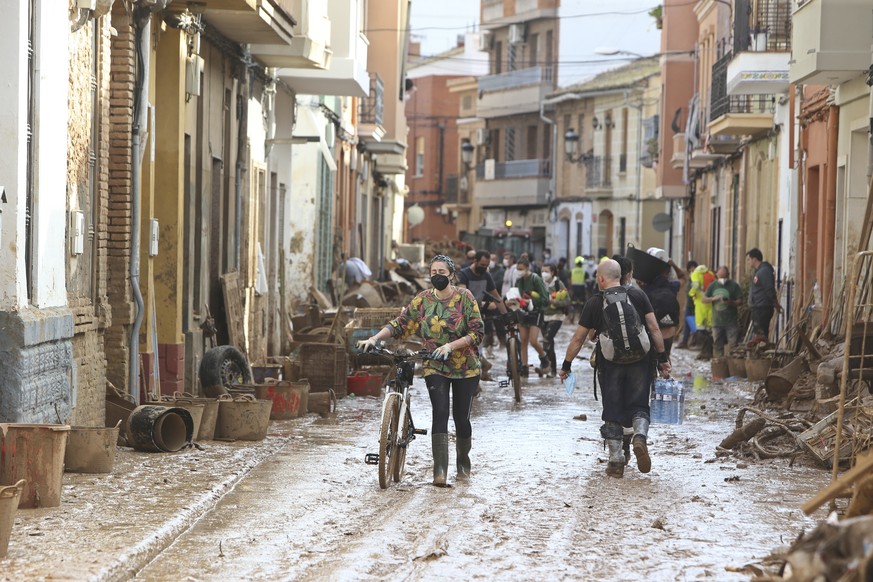 A woman pushes a bicycle along a muddy street after floods in Paiporta, near Valencia, Spain, Sunday, Nov. 3, 2024. (AP Photo/Hugo Torres)