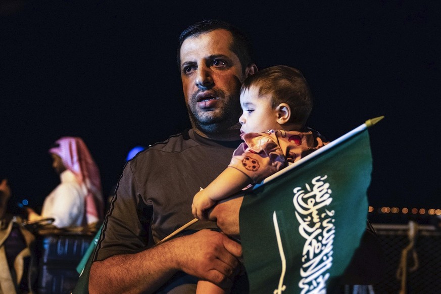 In this photo provided by Saudi Ministry of Media, an evacuee holds a child and a Saudi flag as they arrive at Jeddah Port, Saudi Arabia, Monday, April 24, 2023, after being evacuated from Sudan to es ...