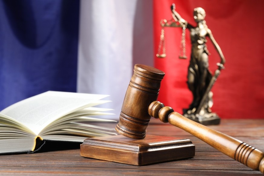 Gavel du juge, livre et statue de la Justice sur une table en bois, avec le drapeau français en arrière-plan.