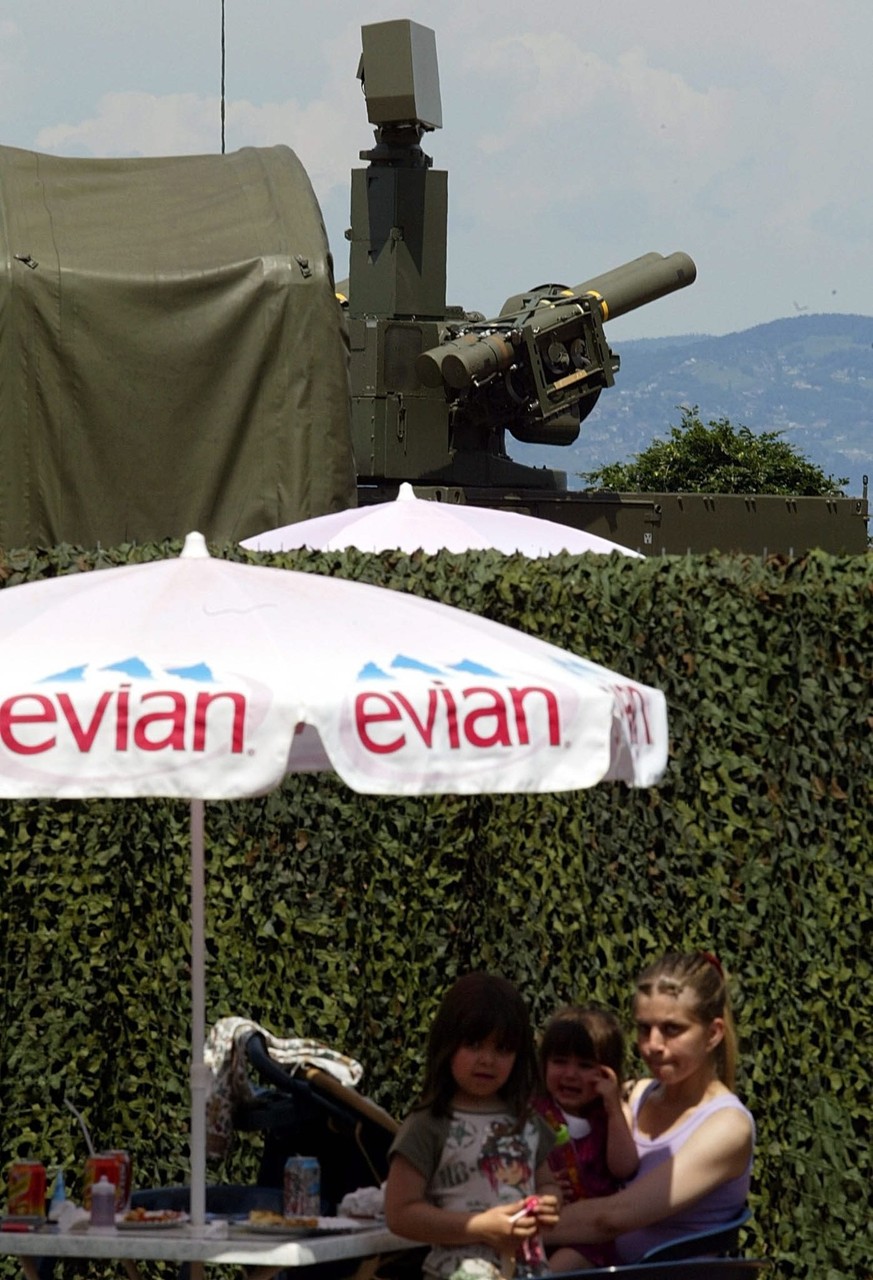 Locals enjoy refreshments next to a temporary military zone with a French military rocket launcher overlooking Lake Geneva from the shores in Evian, Saturday, 31 May 2003. The security has been steppe ...