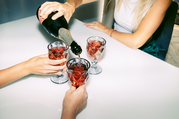Unrecognizable female friends celebrate and drink red sparkling wine