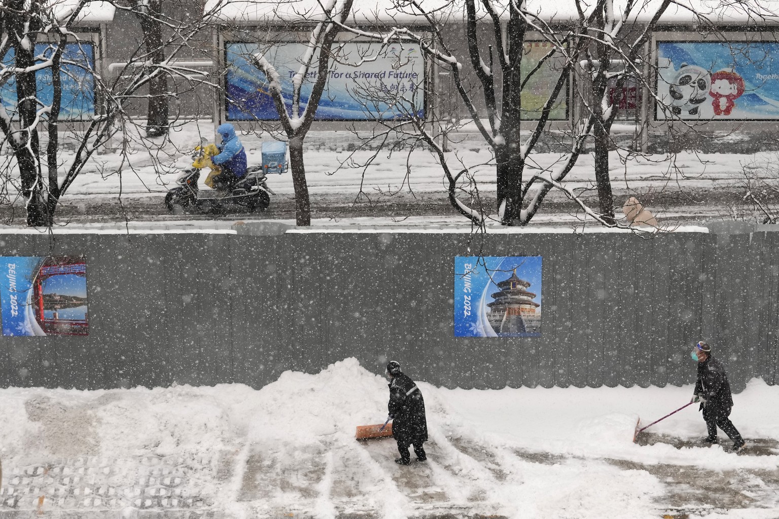 Men clear off snow in front of a hotel at the 2022 Winter Olympics, Sunday, Feb. 13, 2022, in Beijing. (AP Photo/Petr David Josek)