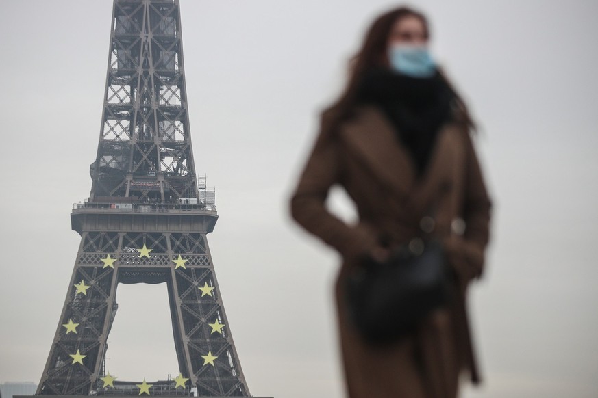 epa09680490 A woman wearing a face mask walks near the Eiffel Tower in Paris, France, 12 January 2022. COVID-19 cases have recorded its highest number daily since the start of the pandemic in France.  ...