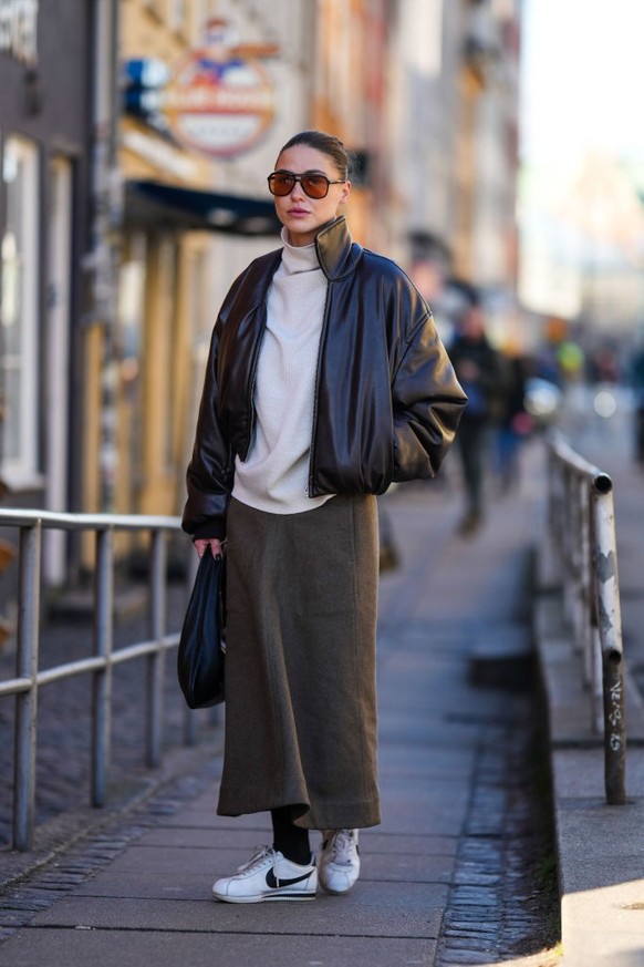 COPENHAGEN, DENMARK - FEBRUARY 02: Sophia Roe wears black sunglasses, a beige wool turtleneck oversized pullover, a black shiny leather bomber coat, dark brown large pants, a black shiny leather handb ...