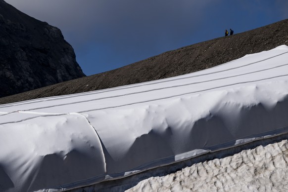 epa10095469 Hikers walk in front of snow from the last winter season covered with blankets to prevent it from melting due to global warming on the Scex Rouge Glacier and Tsanfleuron Glacier at the &#0 ...