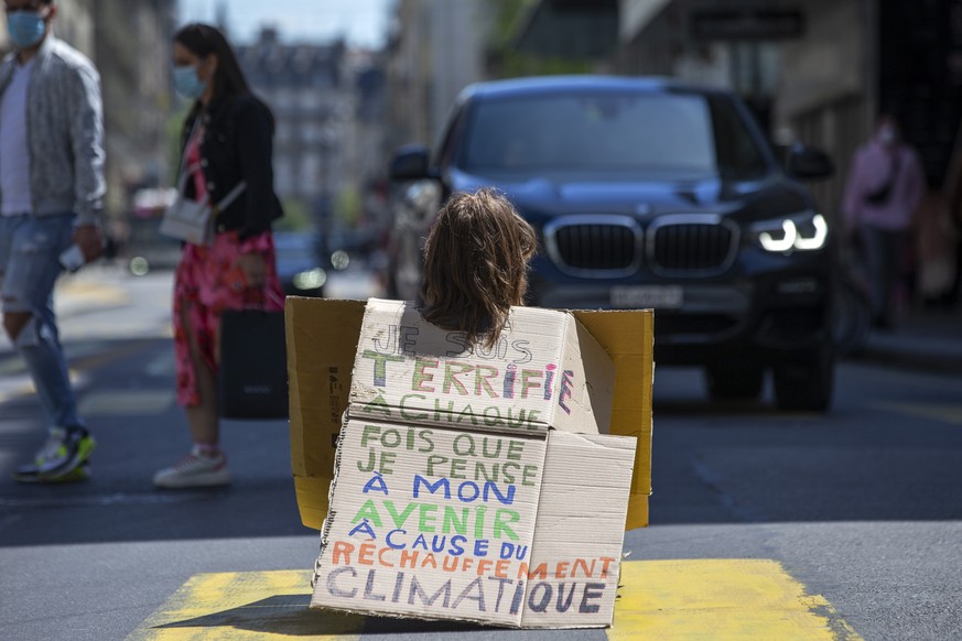 Un militant d&#039;Extinction Rebellion (XR) assis sur la route face a une voiture tenant une pancarte avec le message &quot;Je suis terrifie a chaque fois que je pense mon avenir a cause du rechaufem ...