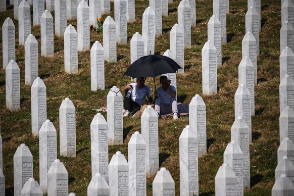 People sit among gravestones at the memorial cemetery in the village of Potocari, near the eastern Bosnian town of Srebrenica, on July 11, 2025, on the 30th anniversary of the Srebrenica massacre.
