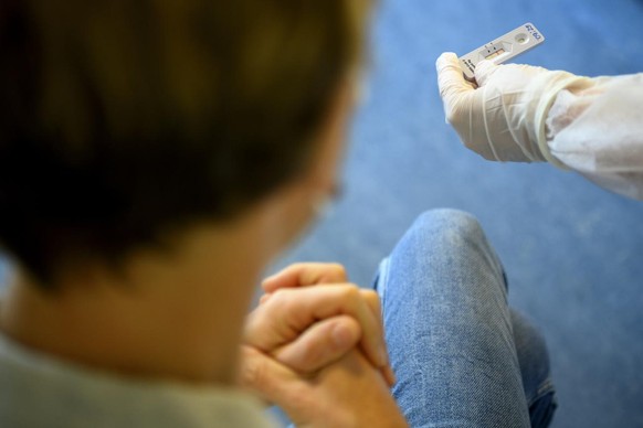 A health worker shows to a patient a positive SARS-CoV-2 Rapid Antigen Test from the Swiss multinational healthcare company Roche just after collecting a nose swab sample for a polymerase chain reacti ...