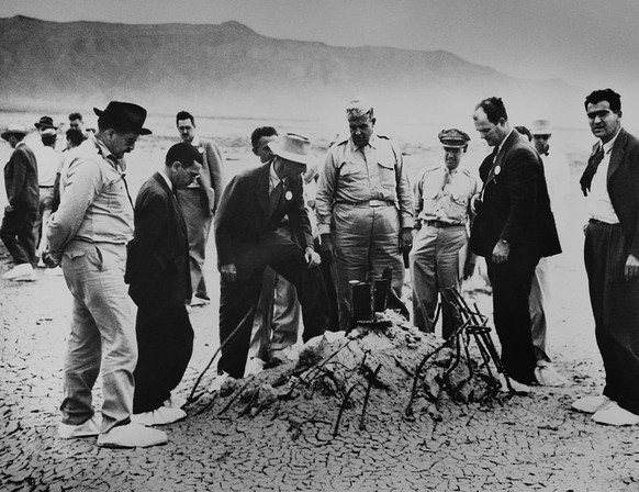 Robert Oppenheimer and General Leslie Groves (center) examine the twisted wreckage that is all that remains of a hundred-foot tower, winch, and shack that held the first nuclear weapon. On the far rig ...