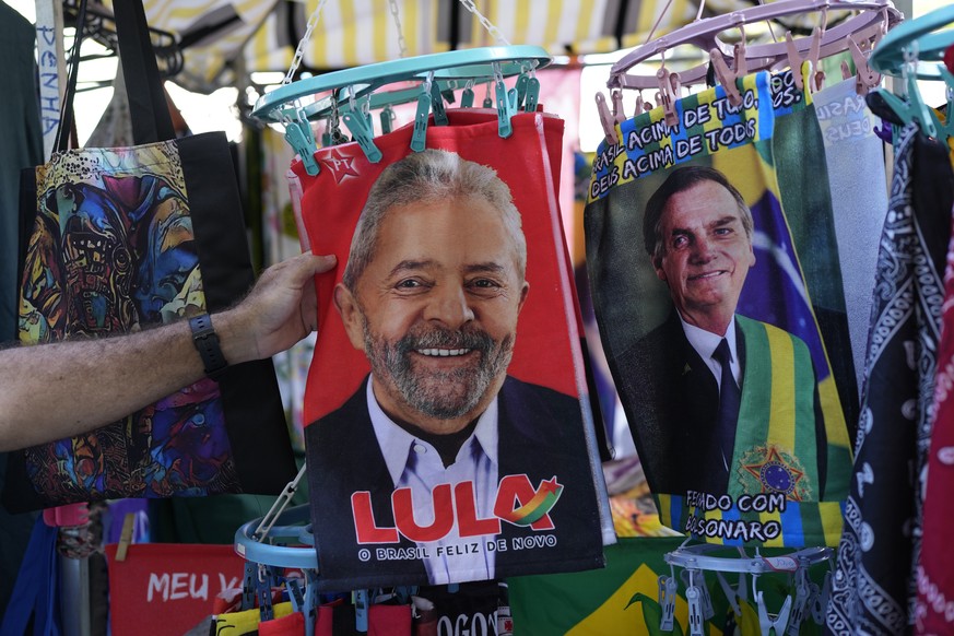 A shopper touches a small towel featuring presidential candidate Luiz Inacio da Silva, or Lula, for sale next to one of Brazilian President Jair Bolsonaro who is running for reelection in Rio de Janei ...
