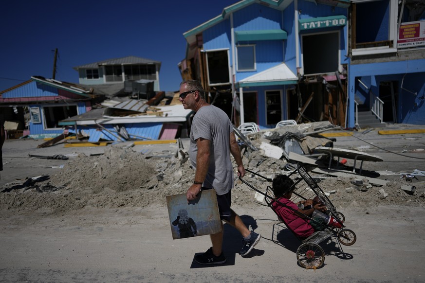 John Quigley carries a piece of artwork made by his daughter, the only thing he found to salvage from his collapsed home, as he pulls his girlfriend&#039;s son Sebastian in a cart while walking off th ...