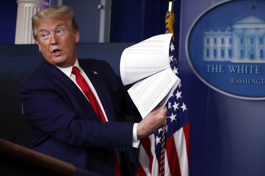 FILE President Donald Trump holds up papers as he speaks about the coronavirus in the James Brady Press Briefing Room of the White House on April 20, 2020, in Washington. Revelations that Trump took g ...