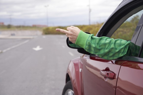Back view of driver shows middle finger throw the window, fuck you with a sign. Concept of road rage.