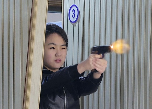 In this photo provided by the North Korean government, its leader Kim Jong Un's daughter, center, tries out a new pistol at a factory producing pistols and other light arms at an undisclosed plac ...
