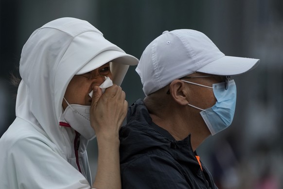 A woman rubs her nose as she rides on an electric bike, crossing an intersection in Beijing, Monday, Aug. 8, 2022. (AP Photo/Andy Wong)